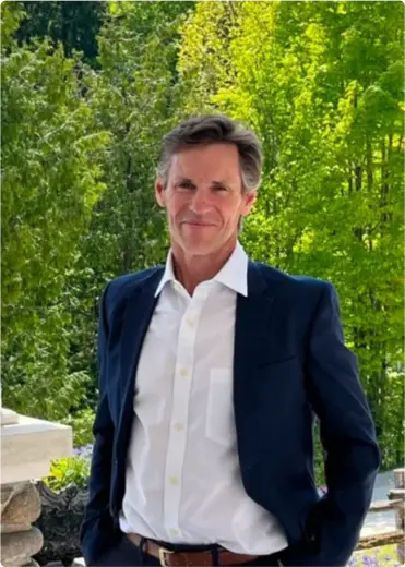 A portrait photo of a man in a suit with trees in the background